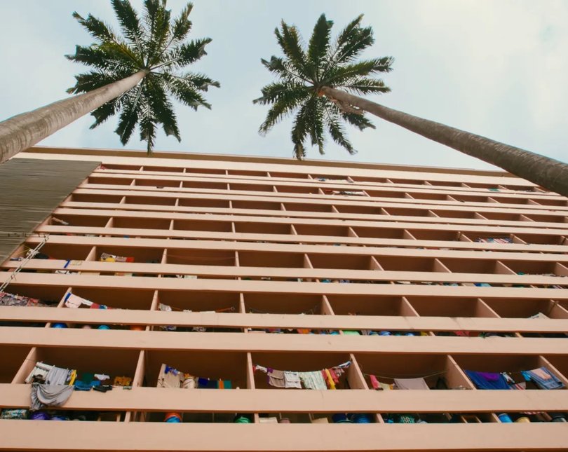A modernist apartment building under two palm trees against a blue sky