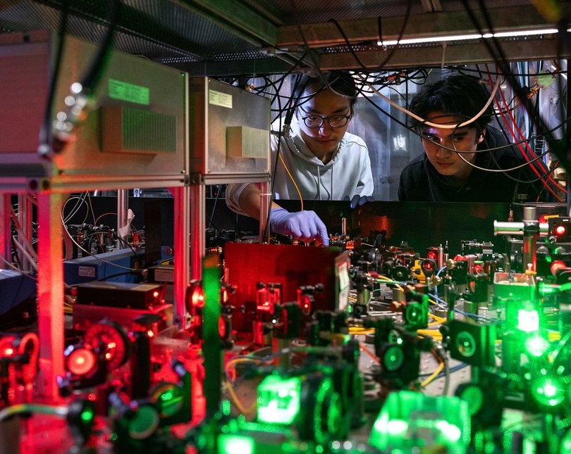 Two science peering inside a machine with lots of wires and lights
