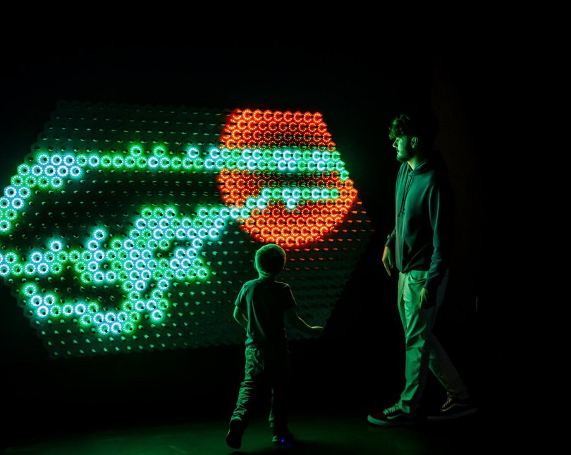 A man and a young boy in front of a glowing LED screen