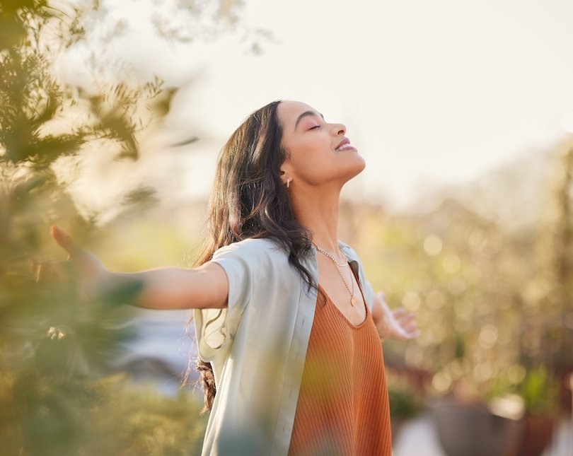 Young brunette walking standing in nature, arms stretched out, looking content