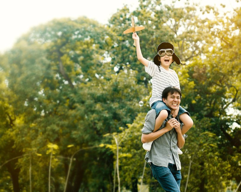 A young boy holding a paper plane sitting on his dad's shoulders