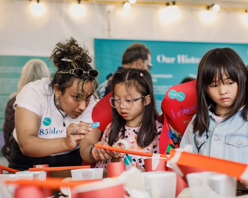 Exhibit volunteer showing objects to two young girls