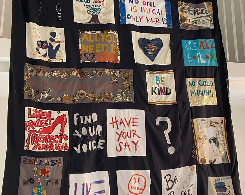 A wall hanging decorated with smaller fabric works showing slogans and messages