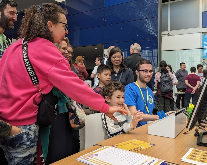 Young child playing a game on a computer with an Imperial researcher helping him