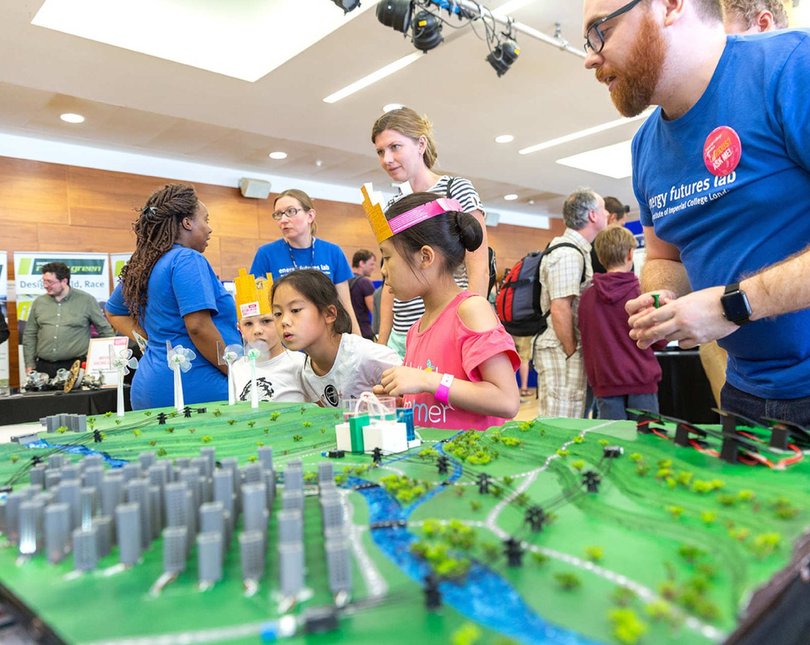 Young children looking at a model of green landscape with wind turbines and other sources of renewable energy