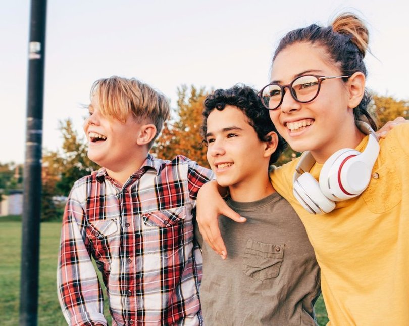 Three young people with their arms around each other smiling outside