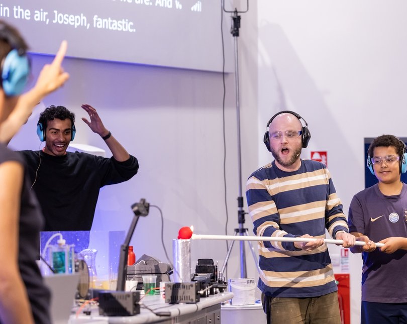 Science show with two male adults and a child conducting an experiment on stage
