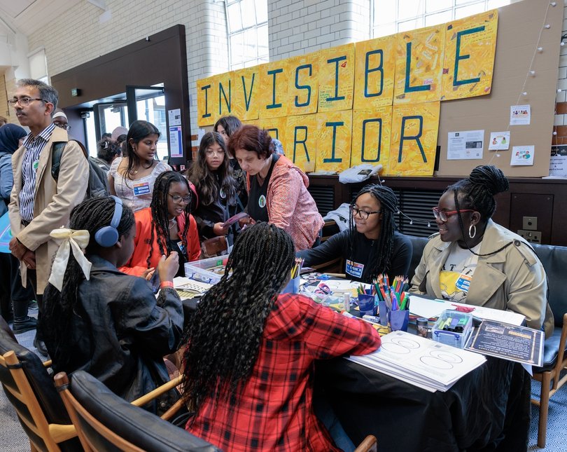 Group of young women doing a crafting workshop in front of a sign that says 'Invisible Warriors'