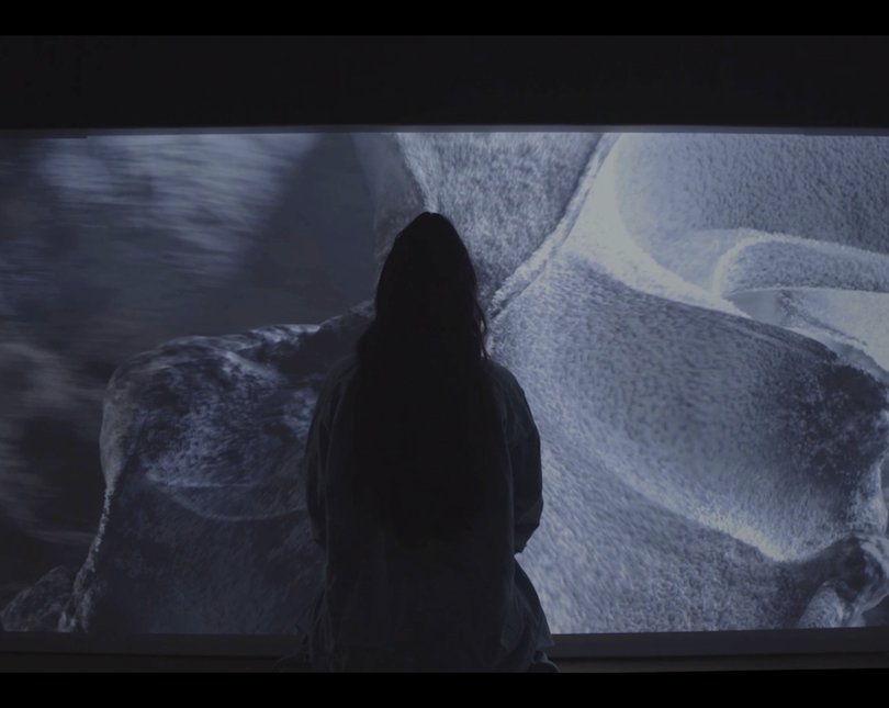 Outline of a woman standing in front of a large screen with swirling patterns