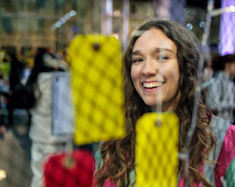 A young woman smiles through the mesh netting of a display